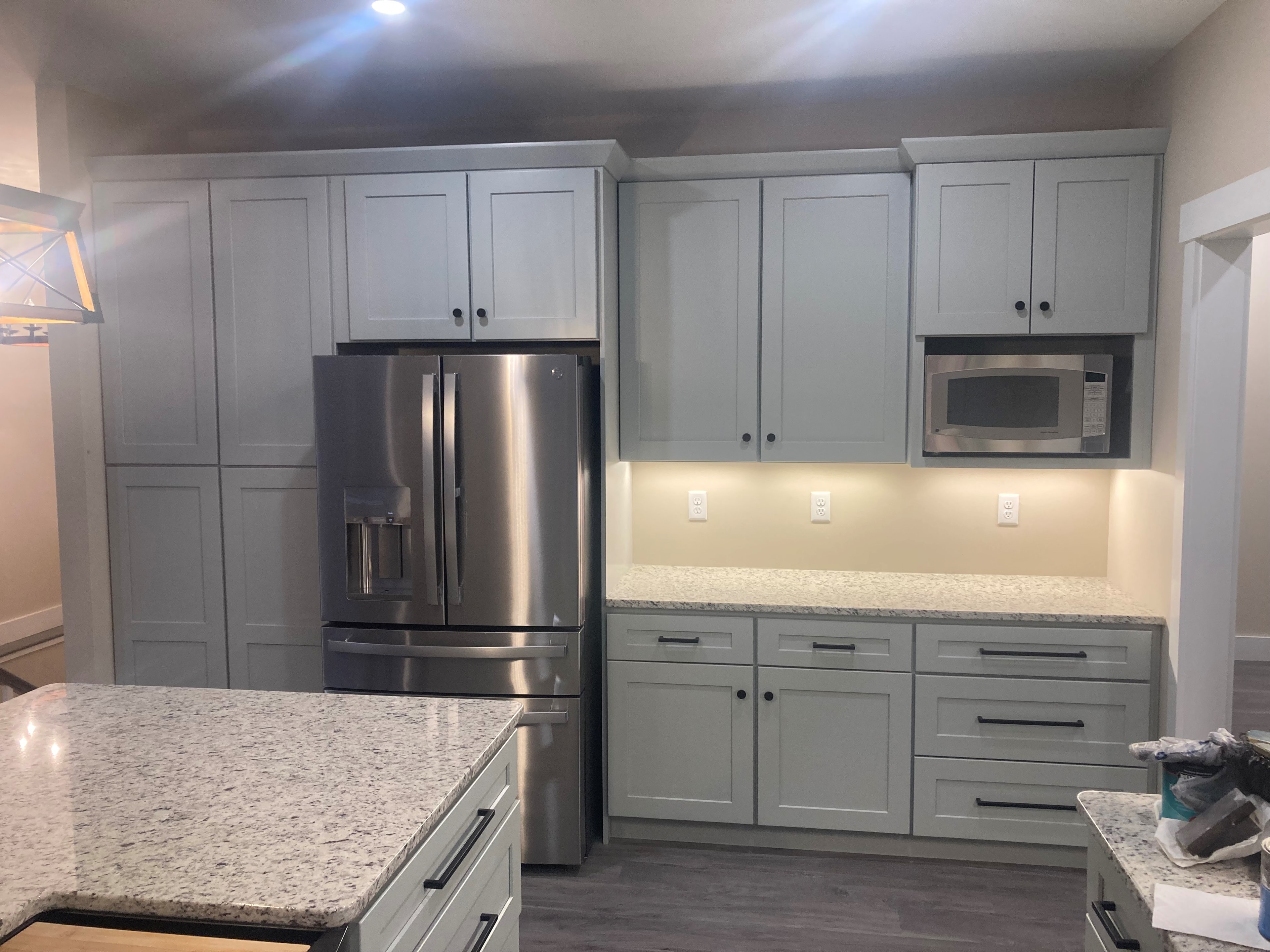 Applewood Estates Home kitchen detail with sage green shaker cabinets, stainless French door refrigerator, granite countertops, and black hardware