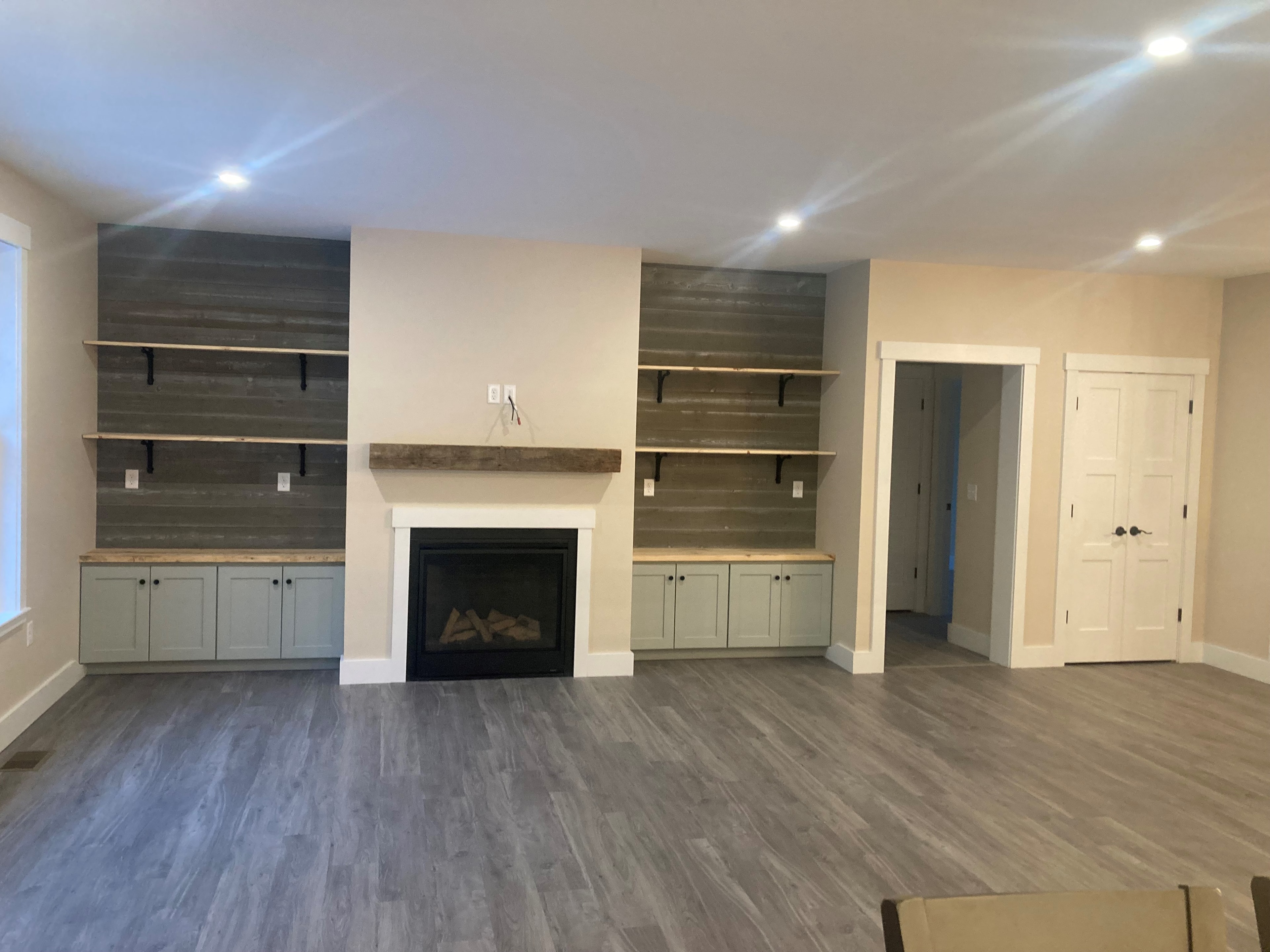 Applewood Estates Home living room with gas fireplace, reclaimed wood shiplap accent wall, open shelving, and sage green built-in cabinets