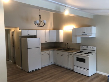 Century Farm Renovations before apartment kitchen with white cabinets, electric range, refrigerator, chandelier, and new LVP flooring — Belmont, NH