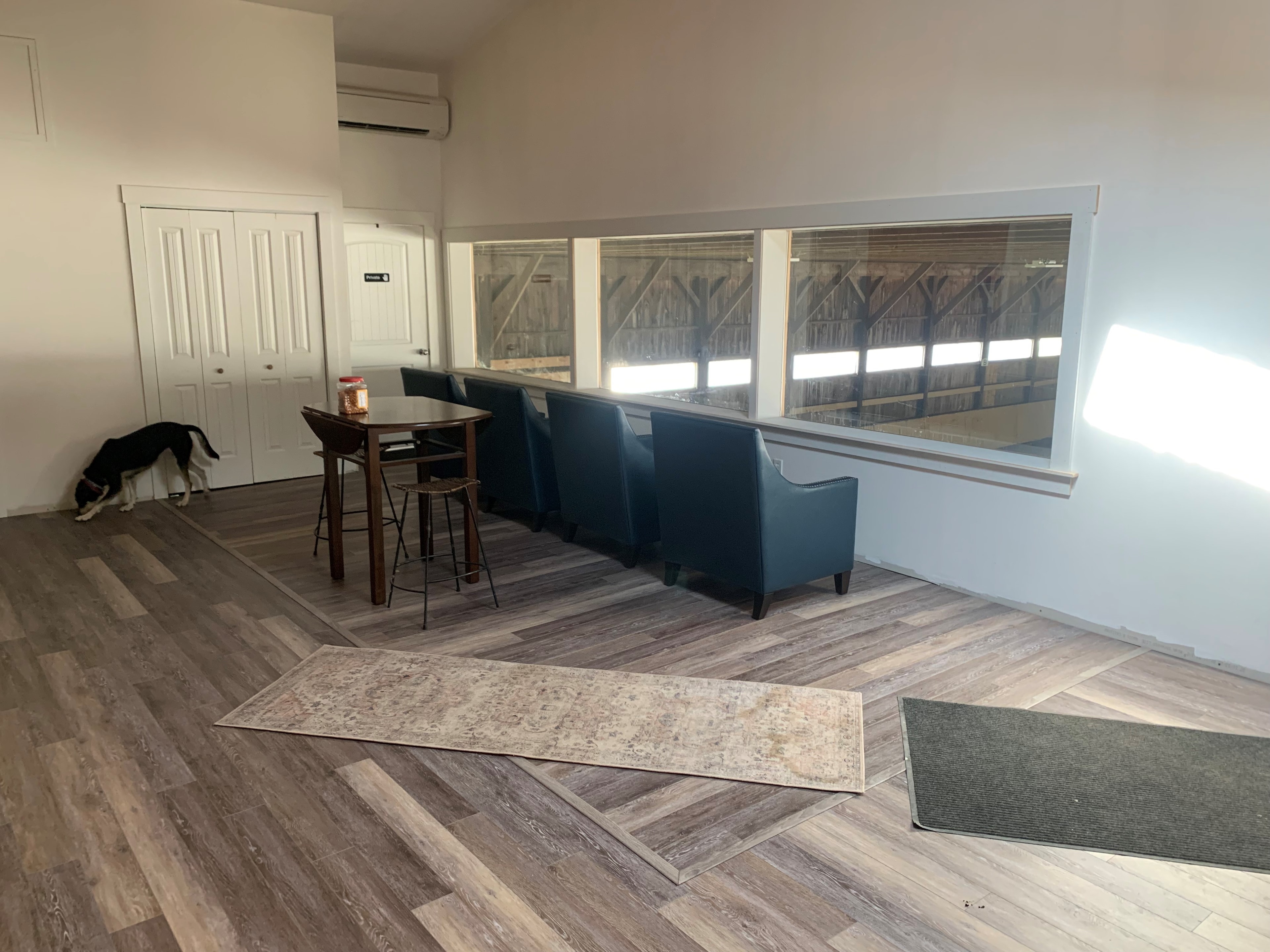 Century Farm Renovations finished viewing room with LVP flooring, blue armchairs, high-top table, and large picture window overlooking the indoor arena — Belmont, NH