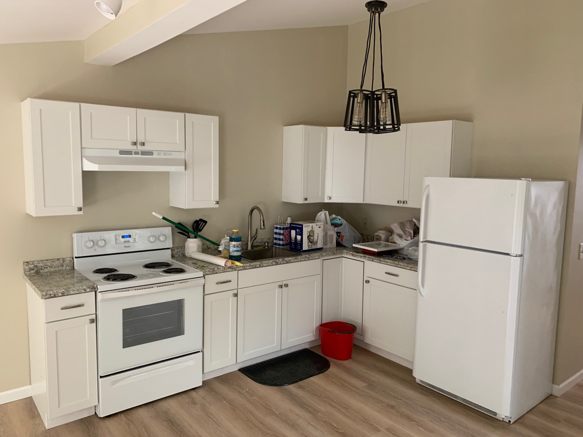 Century Farm Renovations finished apartment kitchen with white shaker cabinets, granite countertops, electric range, refrigerator, and black cage pendant light — Belmont, NH