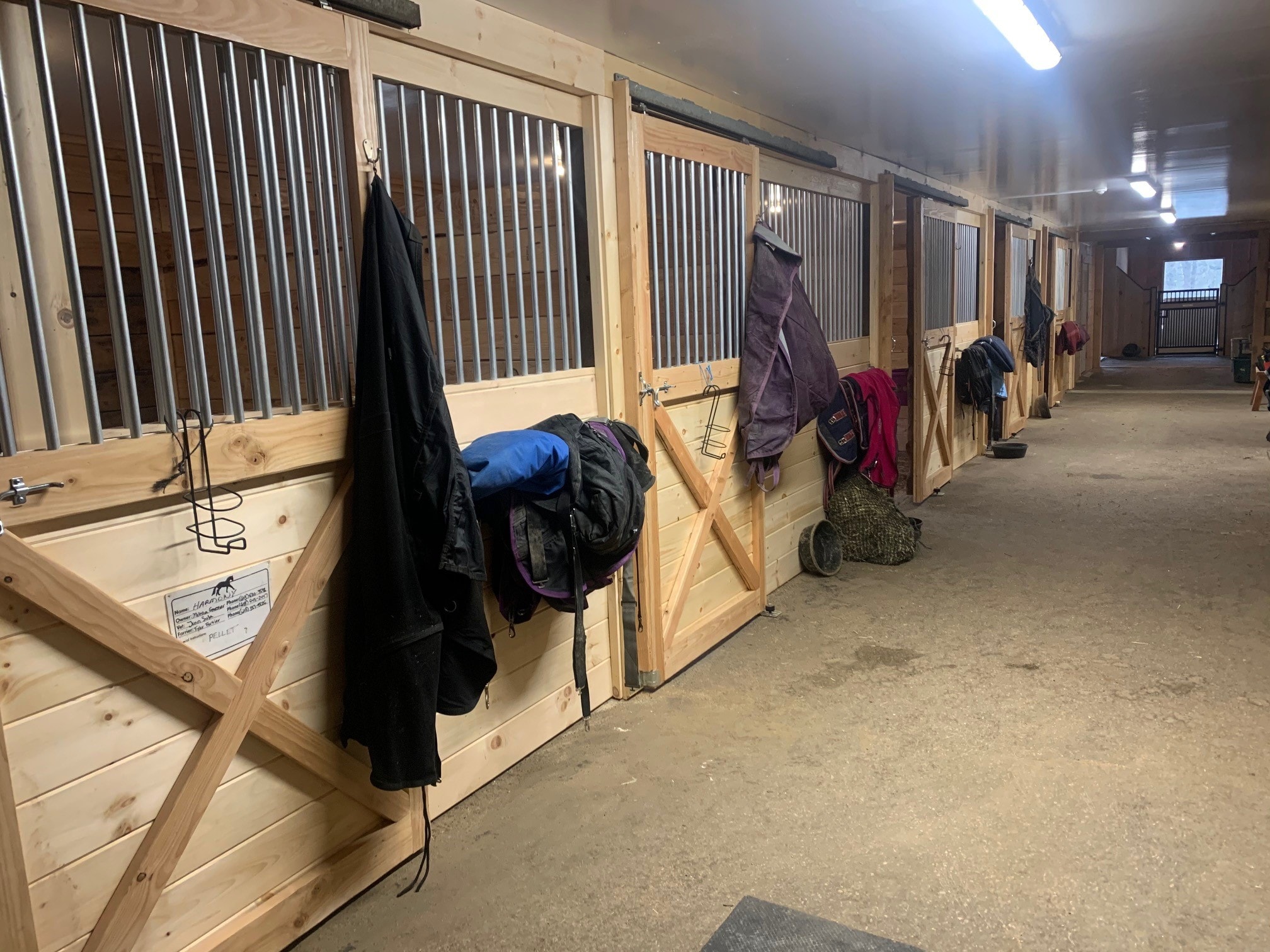 Century Farm Renovations renovated second barn aisle with new pine stall fronts, corrugated metal grilles, horse blankets hung on doors, and LED strip lighting — Belmont, NH