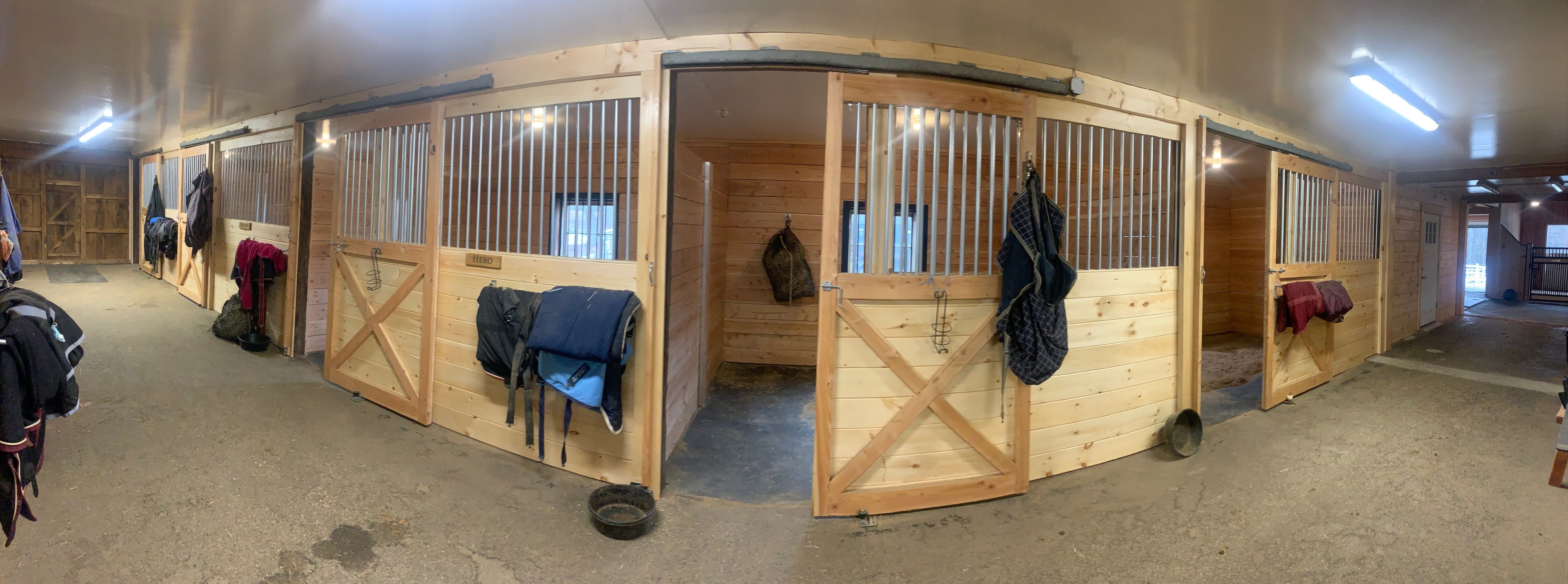 Century Farm Renovations panoramic view of renovated barn with new pine stall fronts, corrugated metal grilles, LED lighting, and open stall door labeled Hero — Belmont, NH
