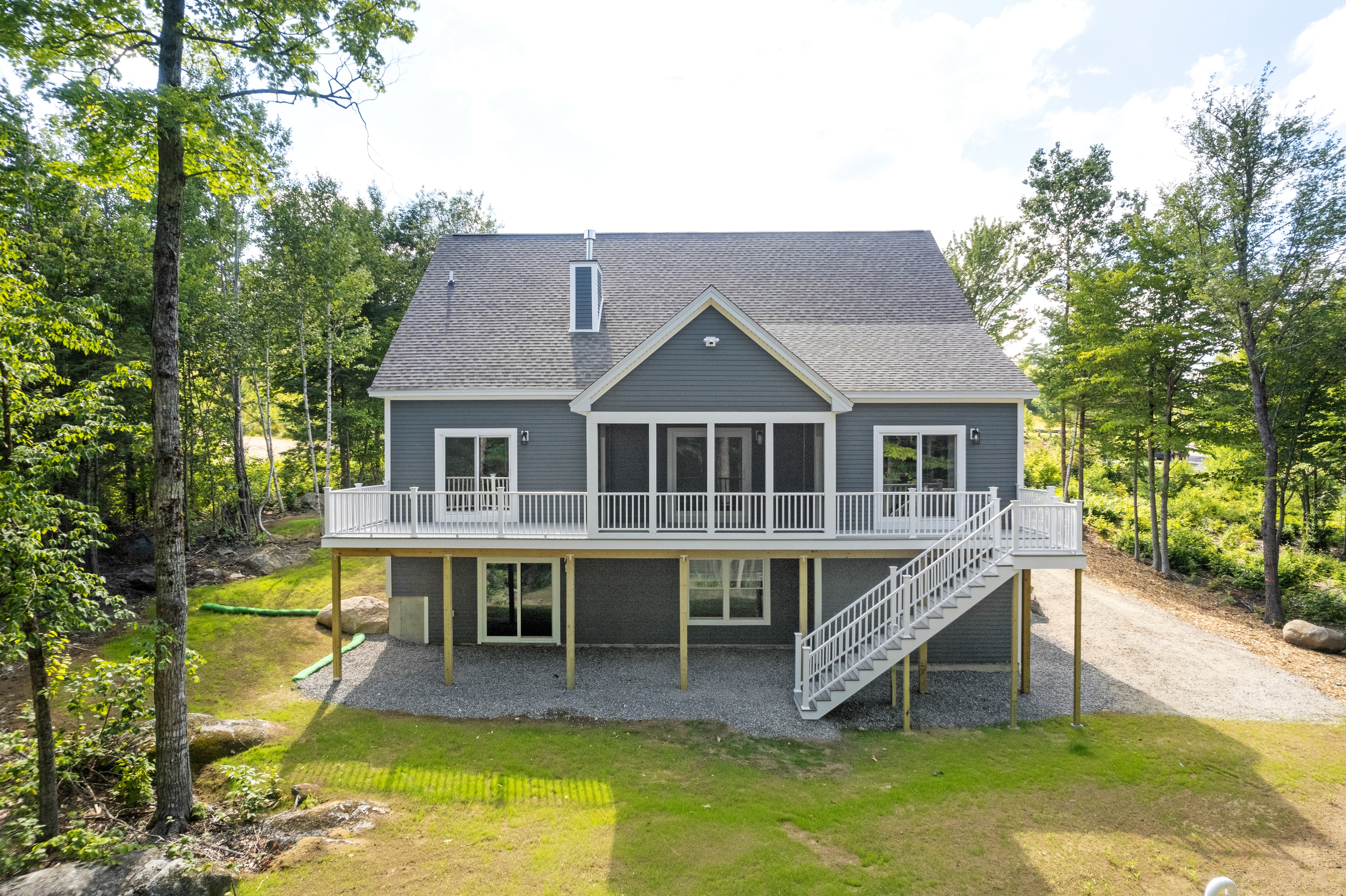 Clover Ridge Home rear exterior with elevated white deck, staircase, walkout lower level, and wooded lot — Meredith, NH