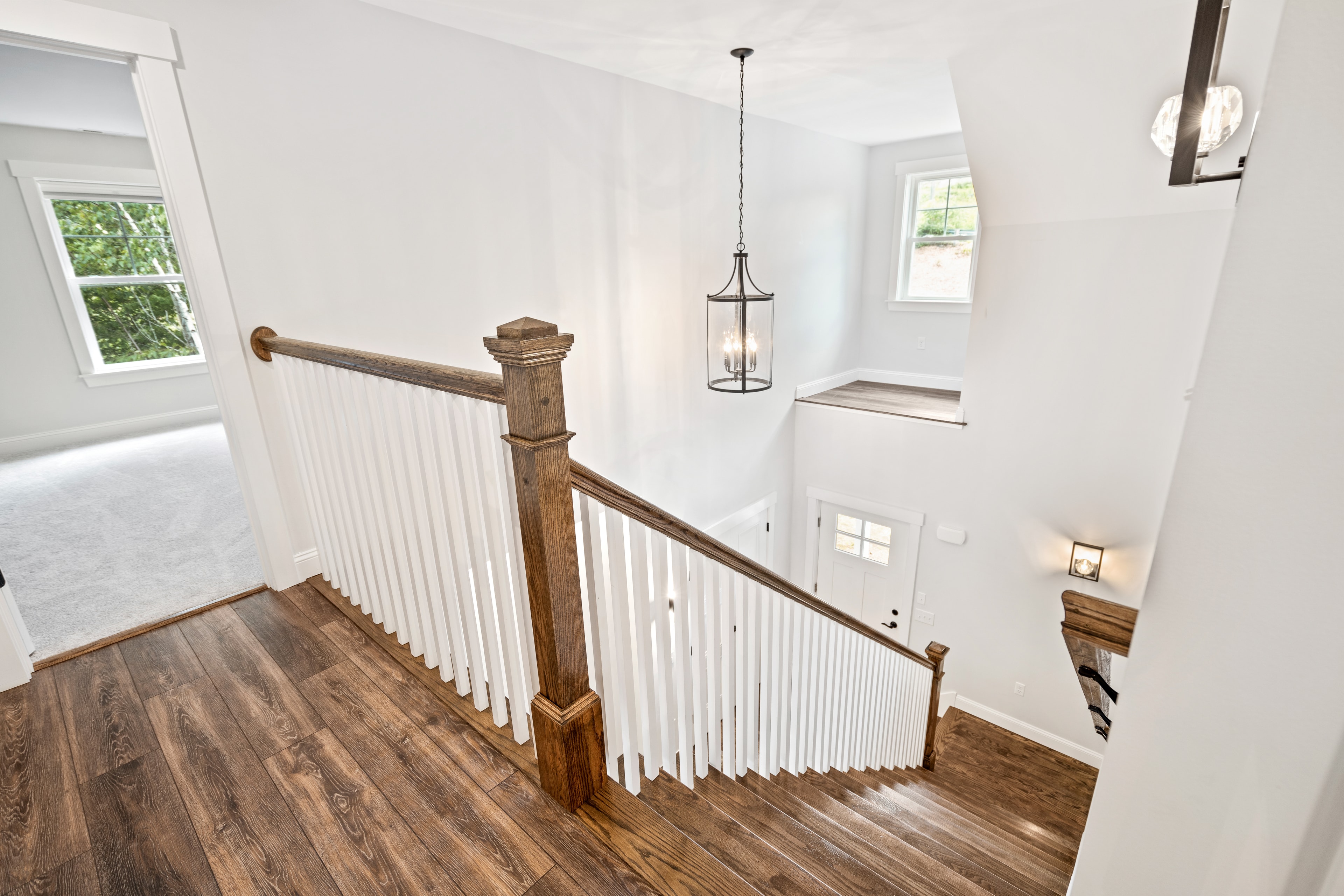 Clover Ridge Home upper landing with wood newel post, white balusters, and lantern pendant light — Meredith, NH