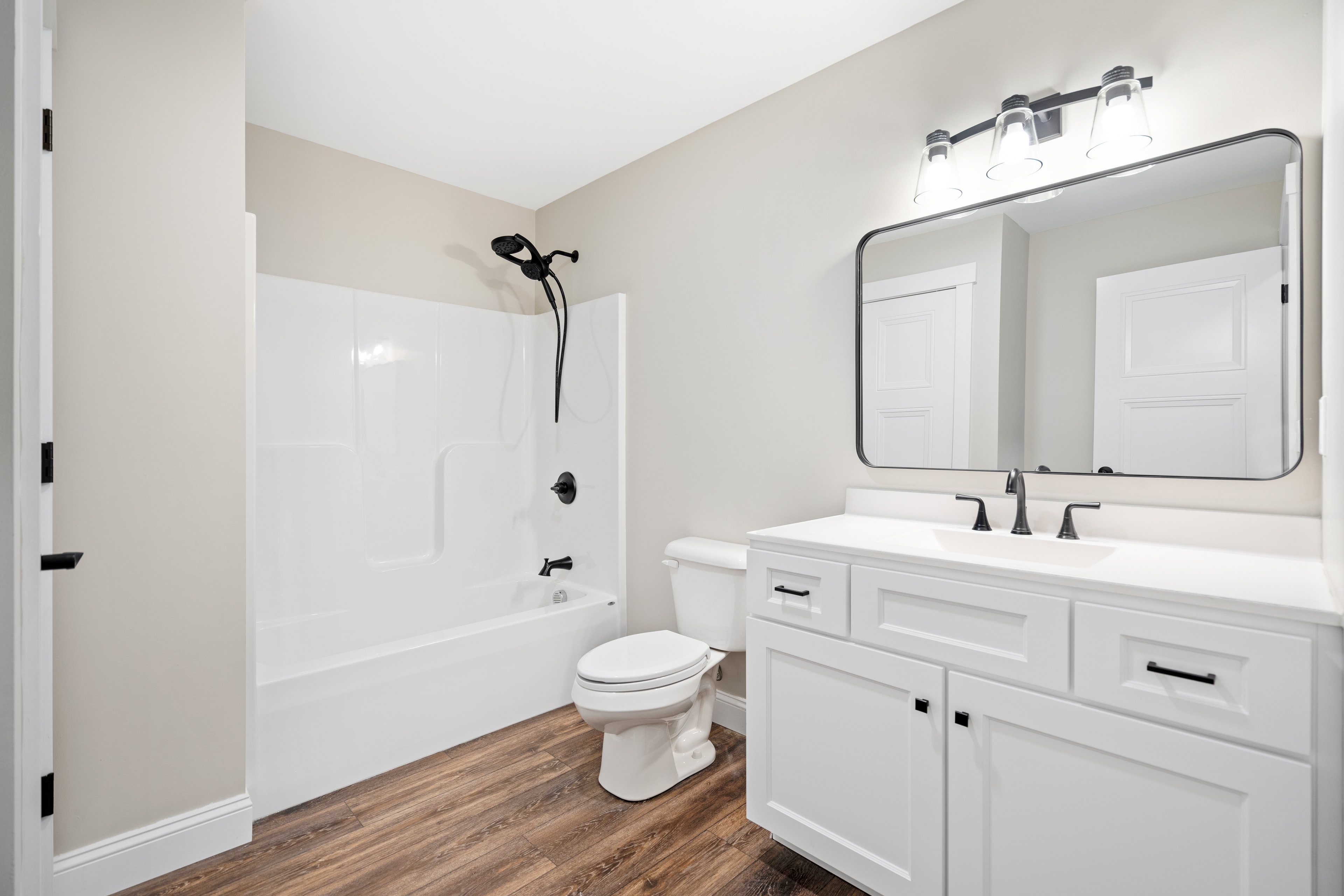 Clover Ridge Home full bath with white shaker vanity, tub-shower combo, black fixtures, and hardwood-look floors — Meredith, NH