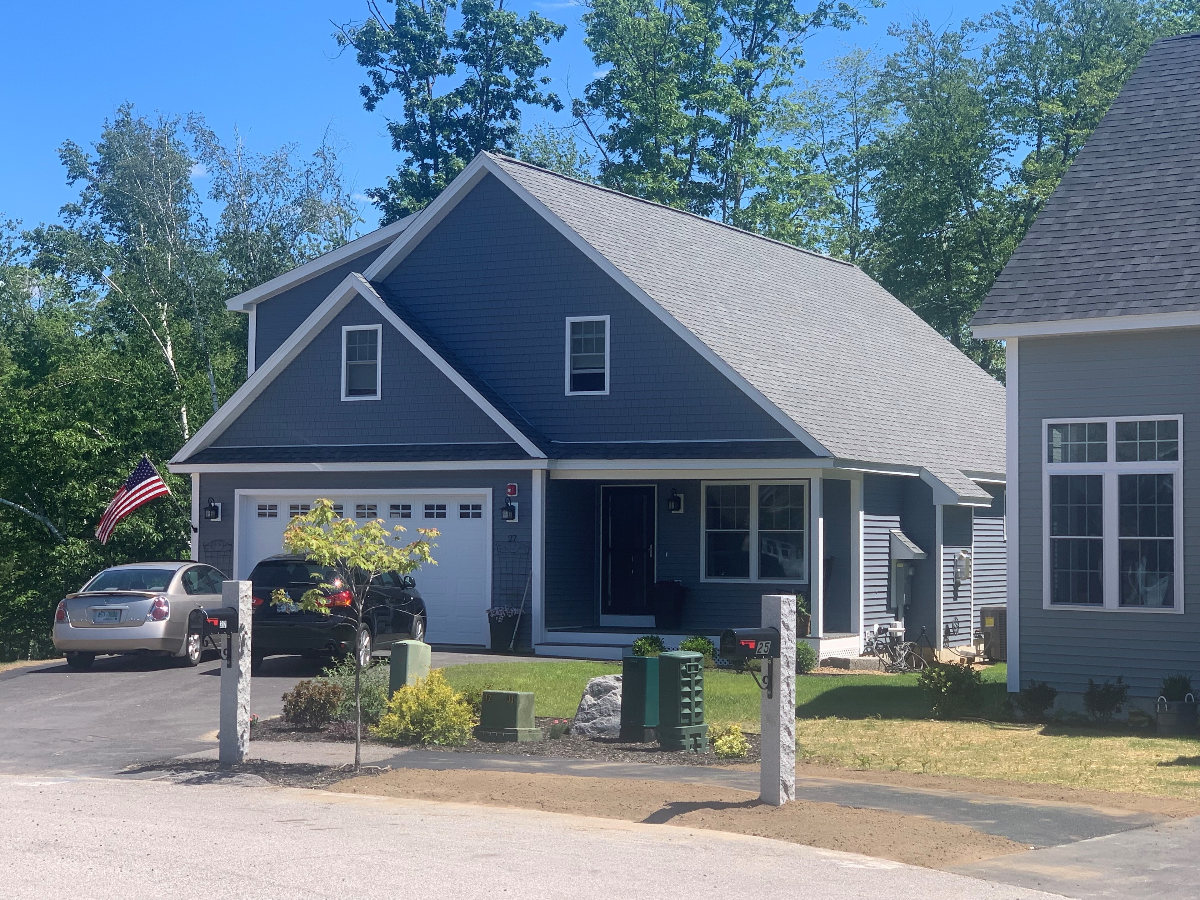 Hawthorn New Build completed summer exterior with slate-blue siding, white trim, covered porch, American flag, and fresh landscaping — Governor's Crossing, NH