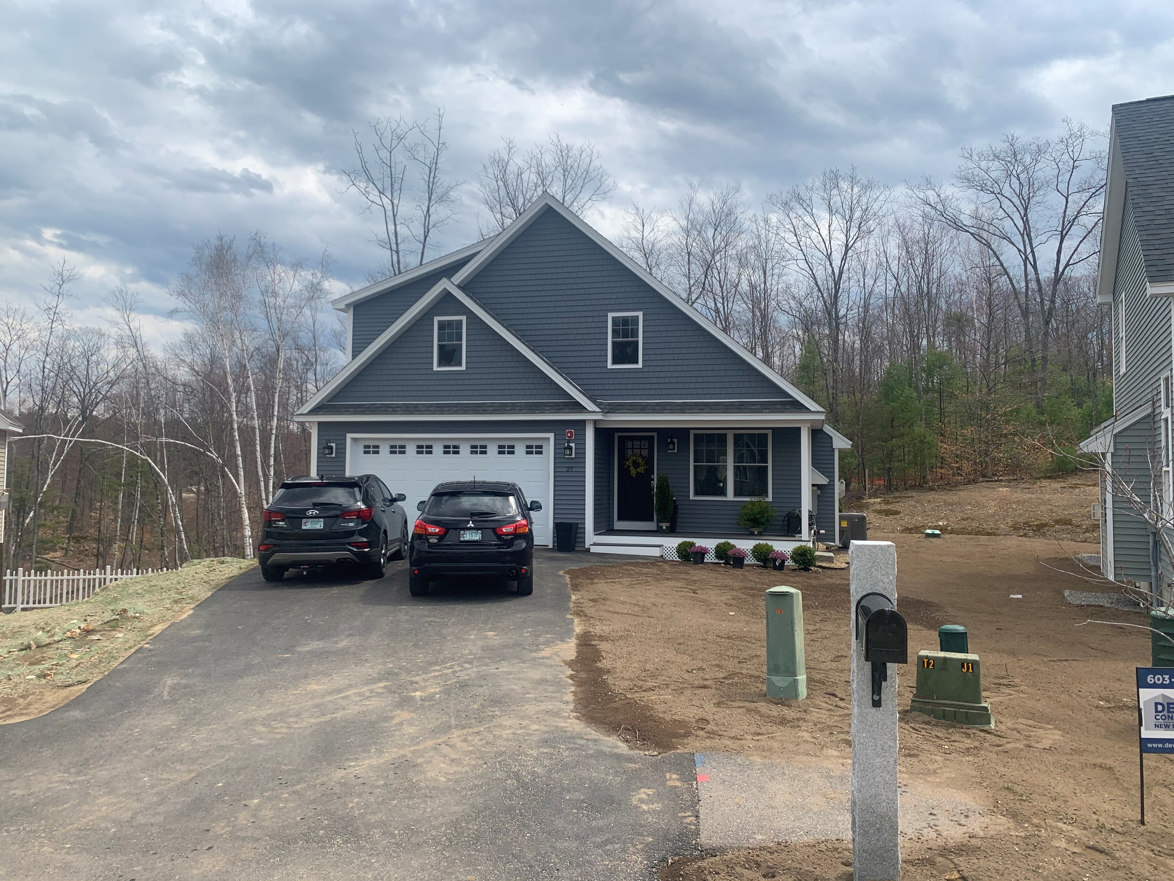 Hawthorn New Build early spring exterior with slate-blue siding, white garage door, two SUVs in driveway, and Deventry Construction sign — Governor's Crossing, NH
