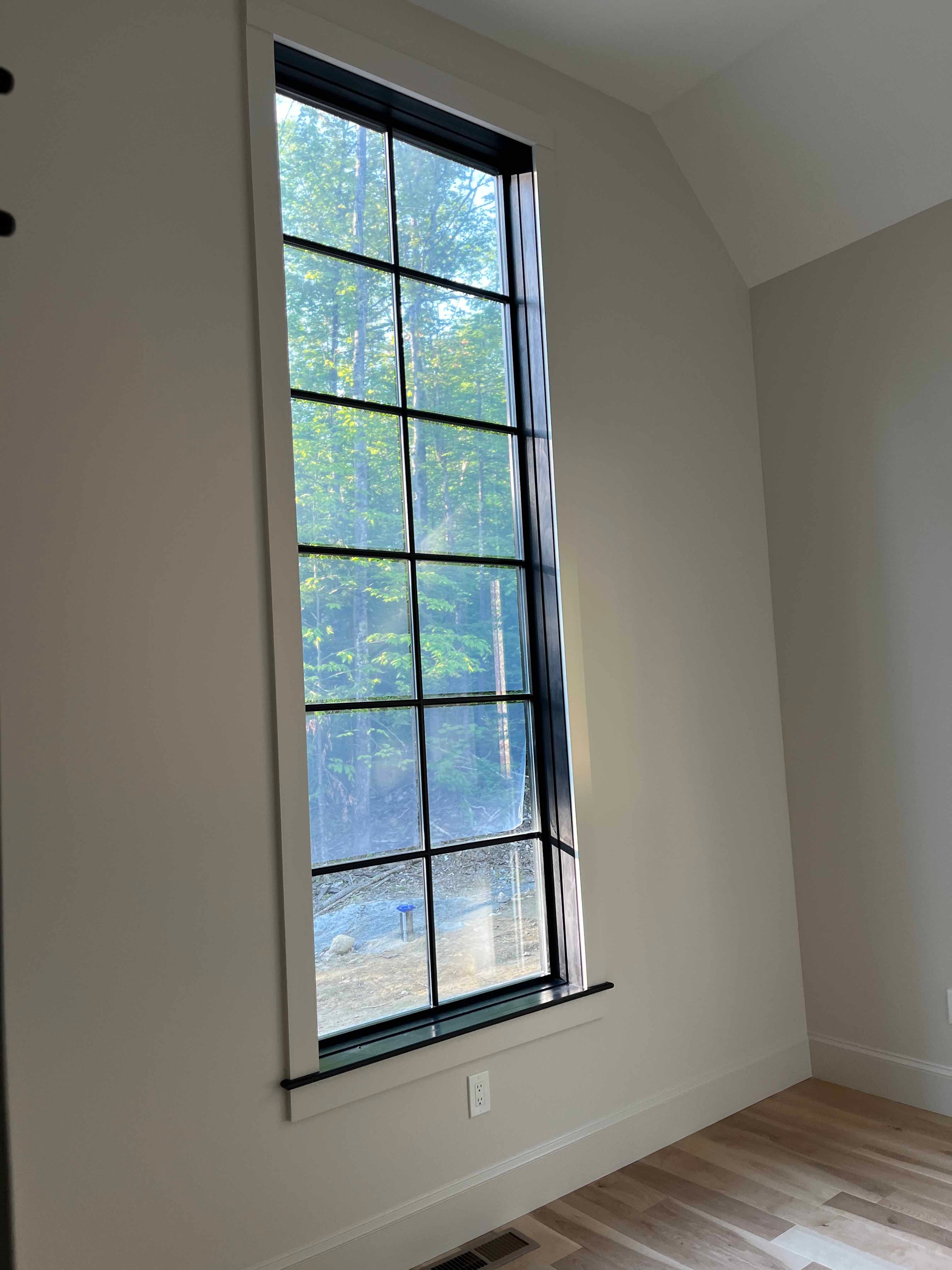 Holderness Home great room with floor-to-ceiling black-framed window overlooking wooded yard
