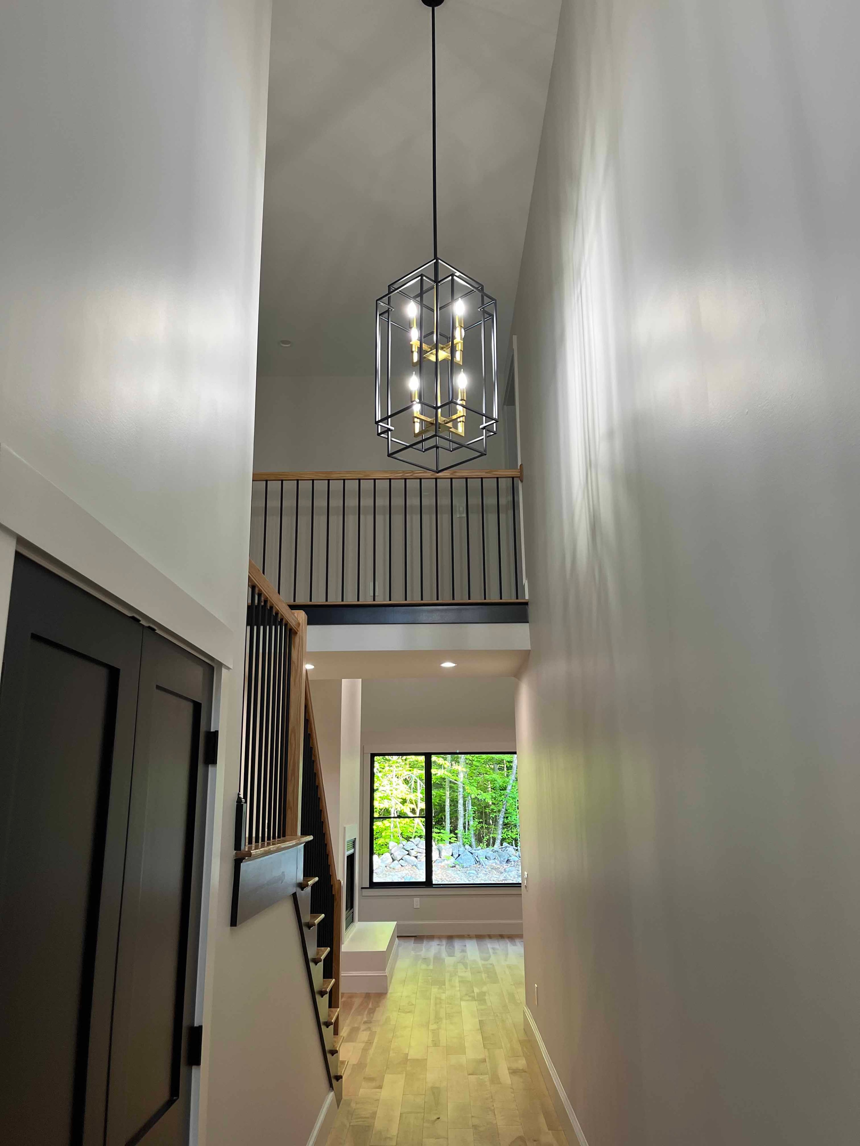 Holderness Home two-story foyer with geometric black-and-gold chandelier, oak stair railing, and black balusters