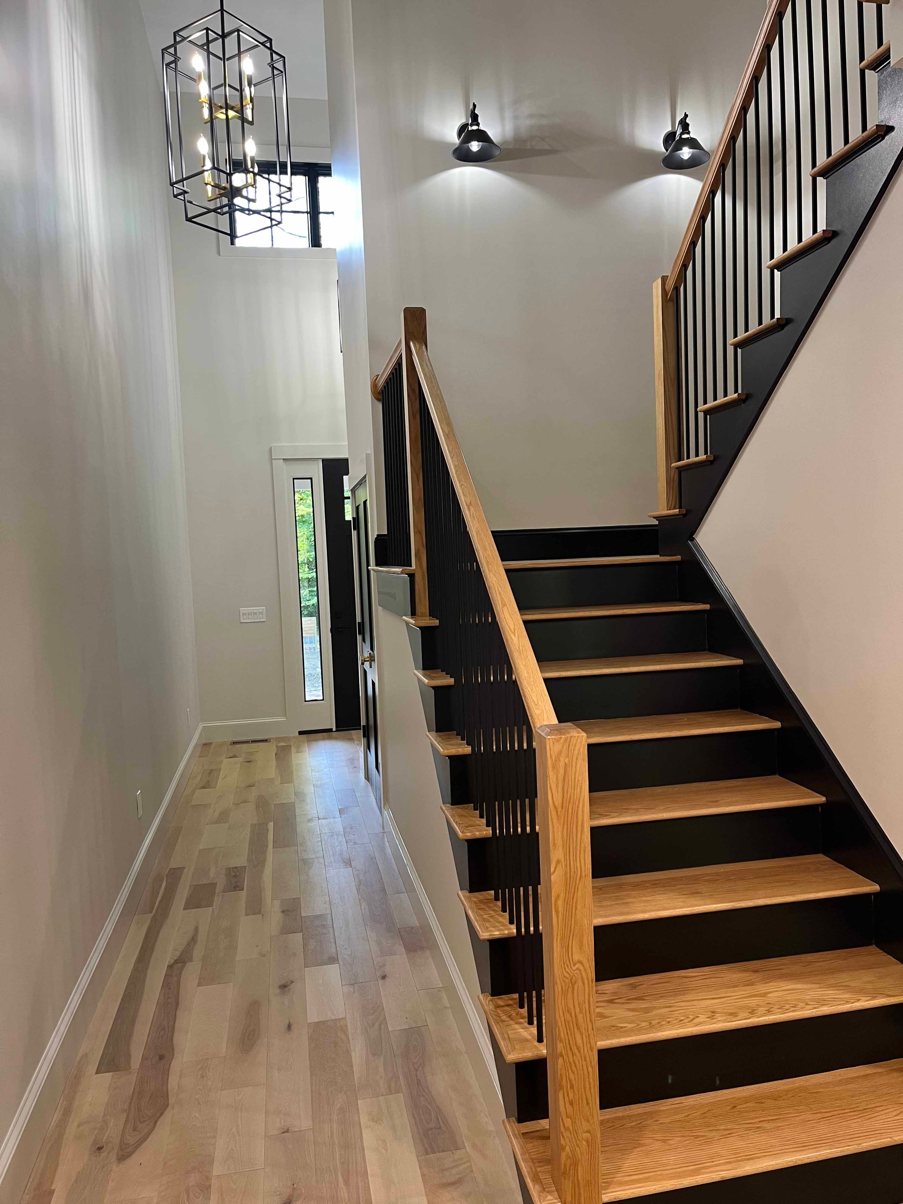 Holderness Home staircase with oak treads, black risers, black balusters, and geometric chandelier above