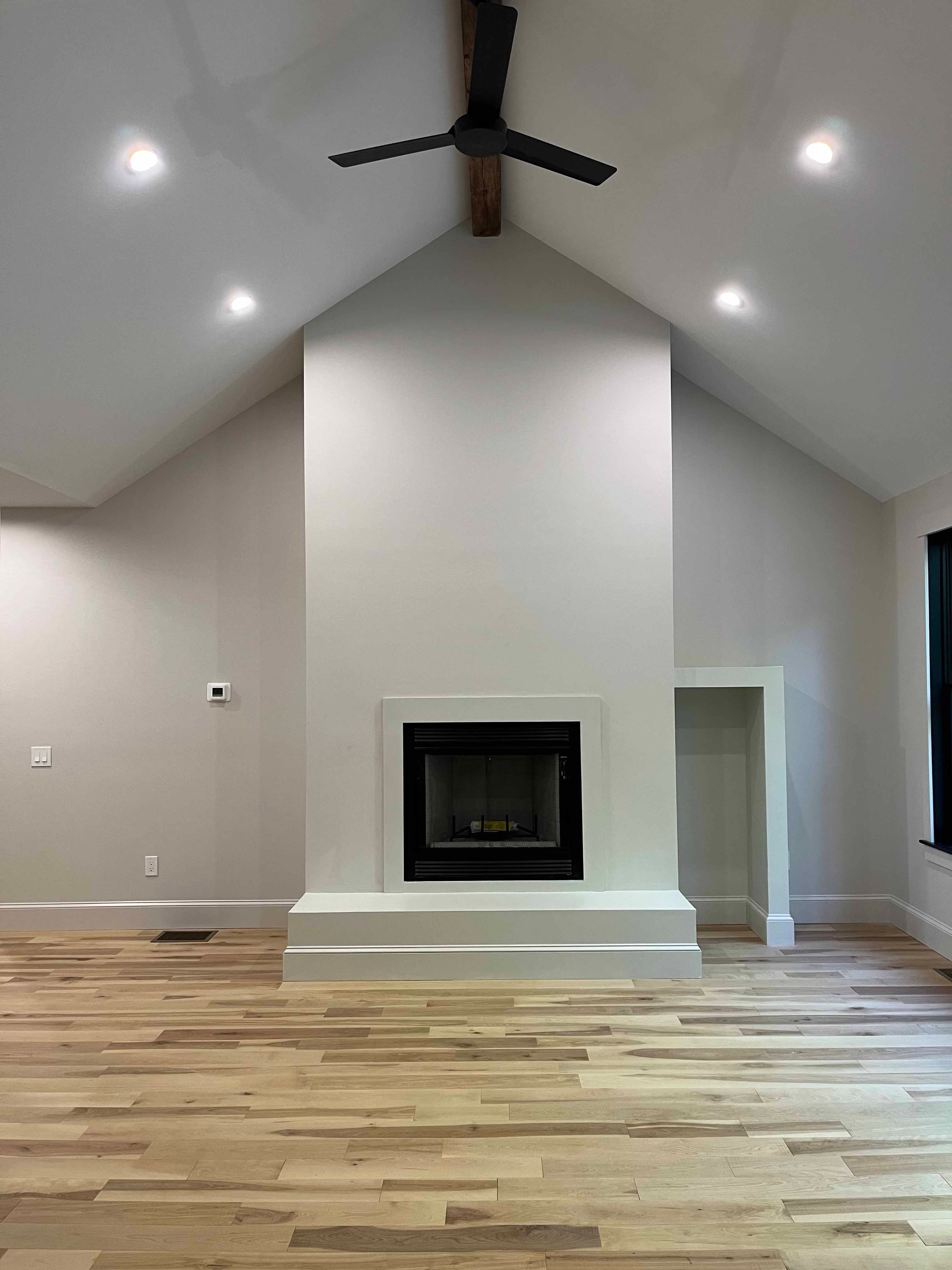 Holderness Home great room with vaulted ceiling, gas fireplace, exposed beam, and black ceiling fan