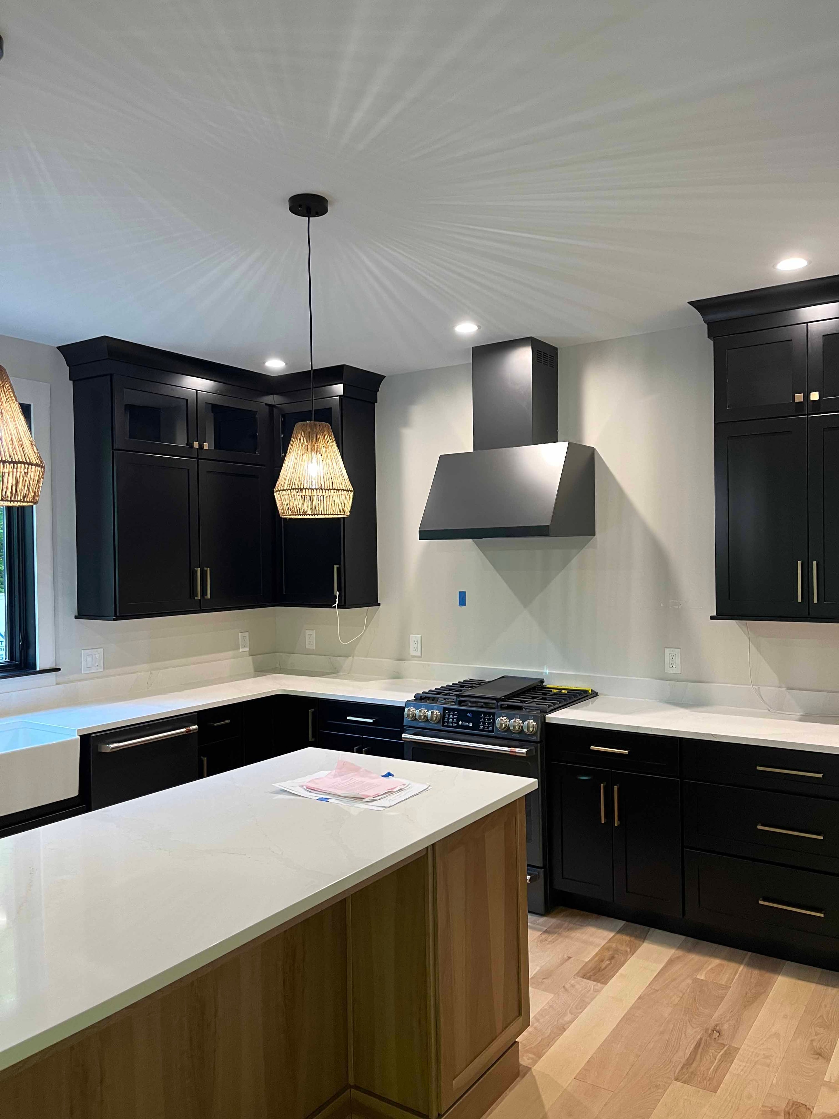 Holderness Home kitchen with black shaker cabinets, white quartz countertops, wood island, rattan pendant, and black range hood