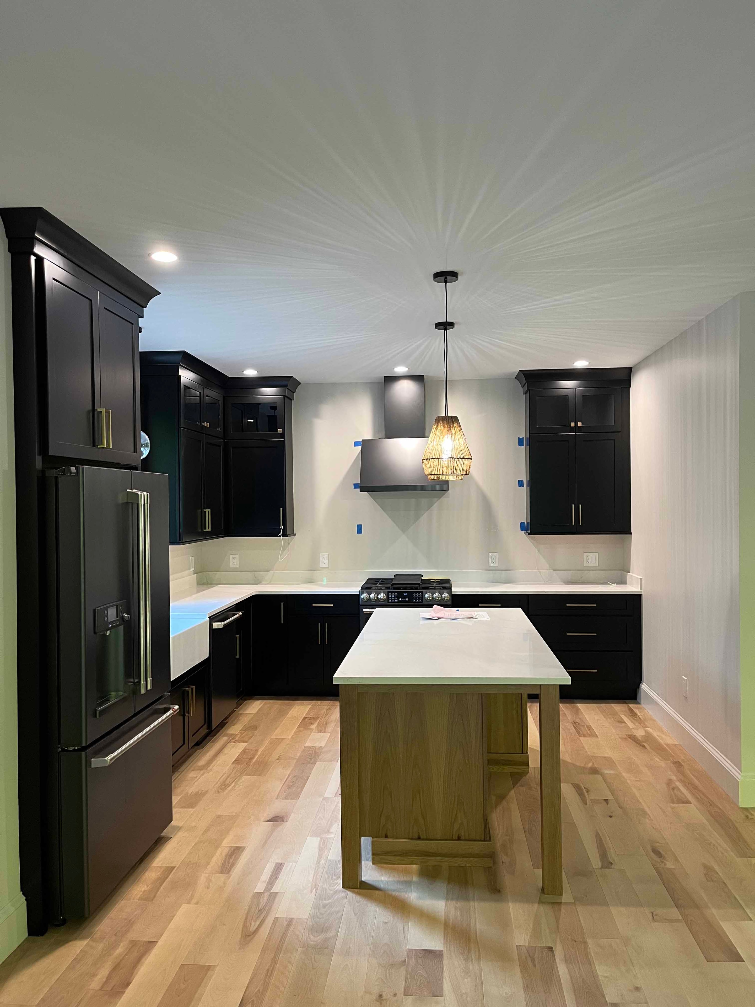 Holderness Home kitchen wide angle with black cabinets, black refrigerator, wood island, and rattan pendant lights
