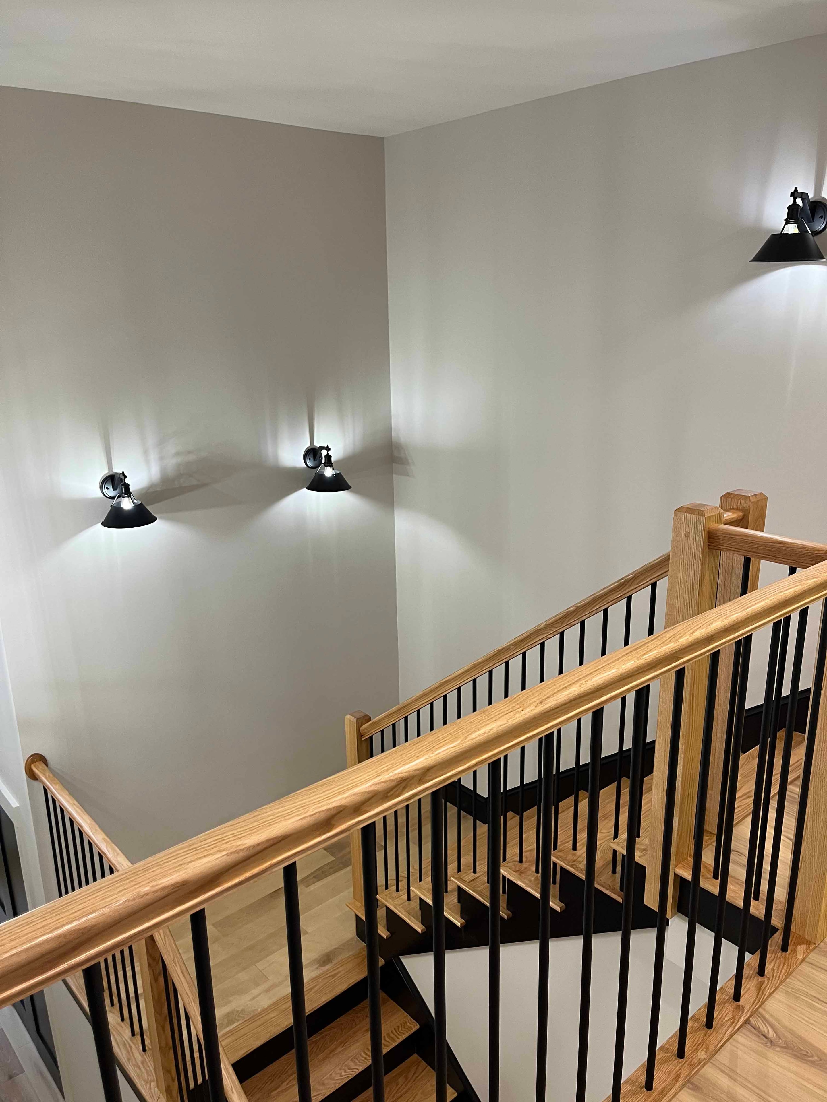 Holderness Home staircase landing with oak railing, black balusters, and black wall sconces