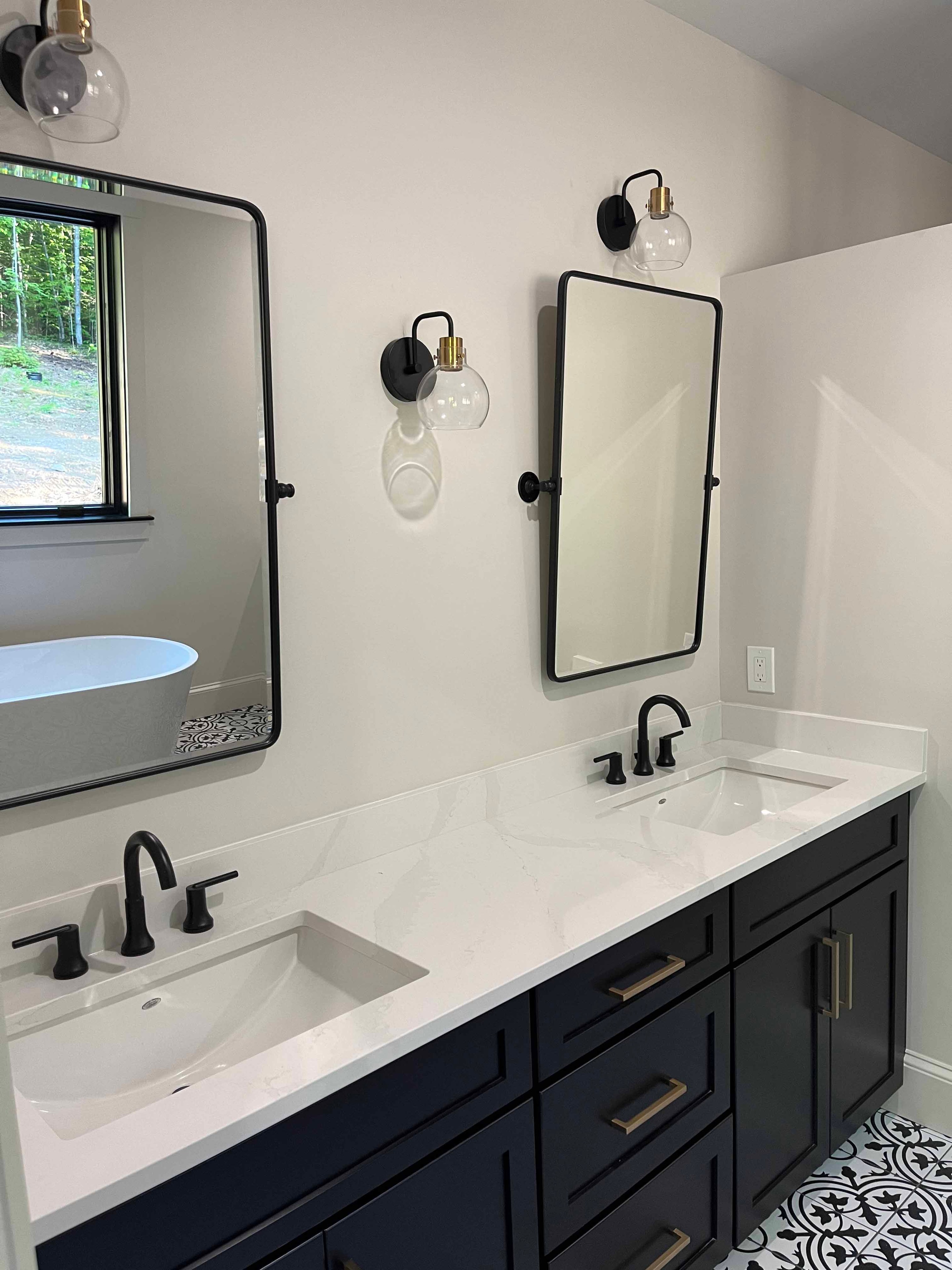 Holderness Home master bath double vanity with navy cabinets, quartz countertop, black mirrors, and globe sconces