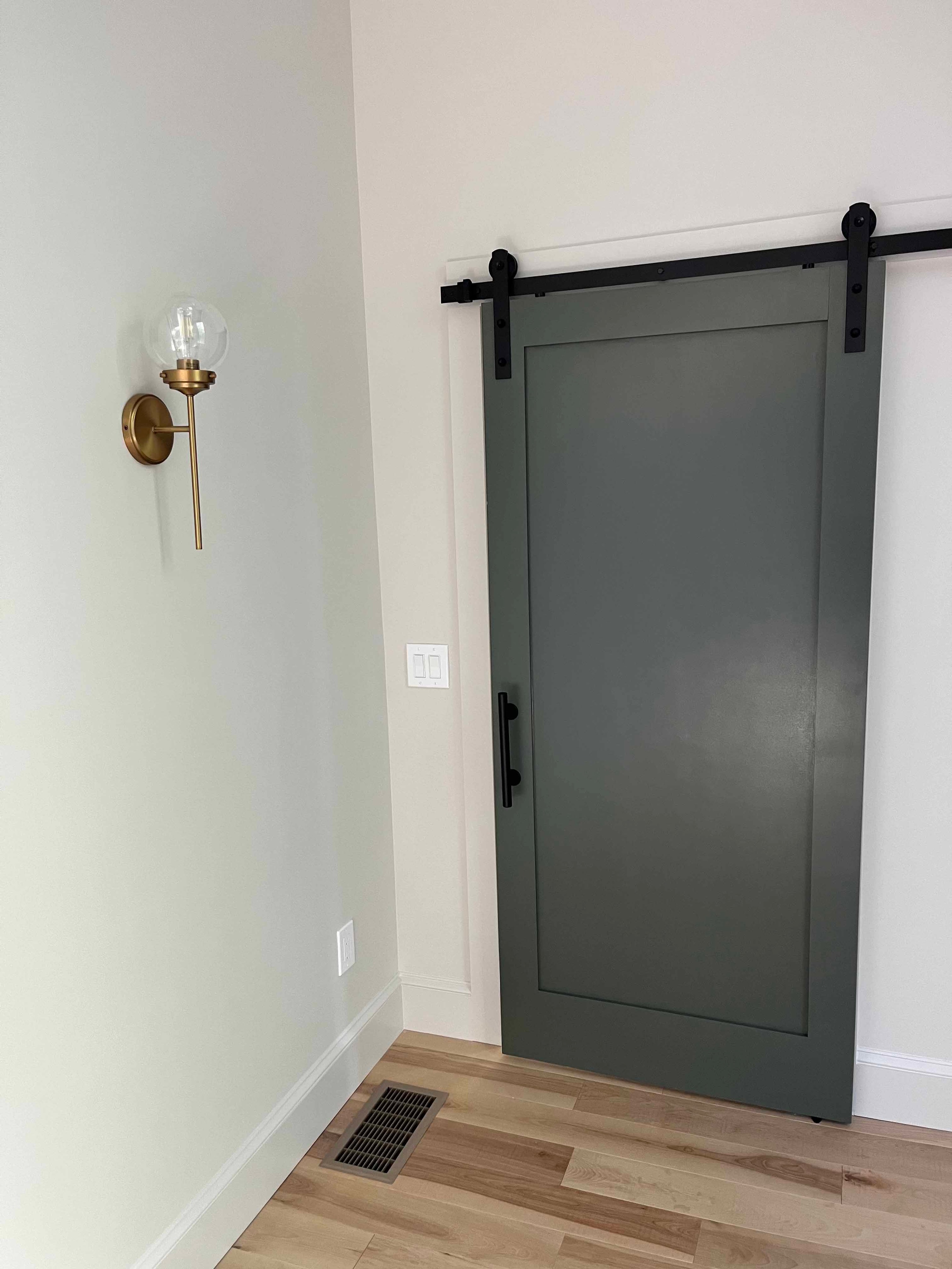 Holderness Home hallway with sage green sliding barn door, brass sconce, and oak hardwood floors
