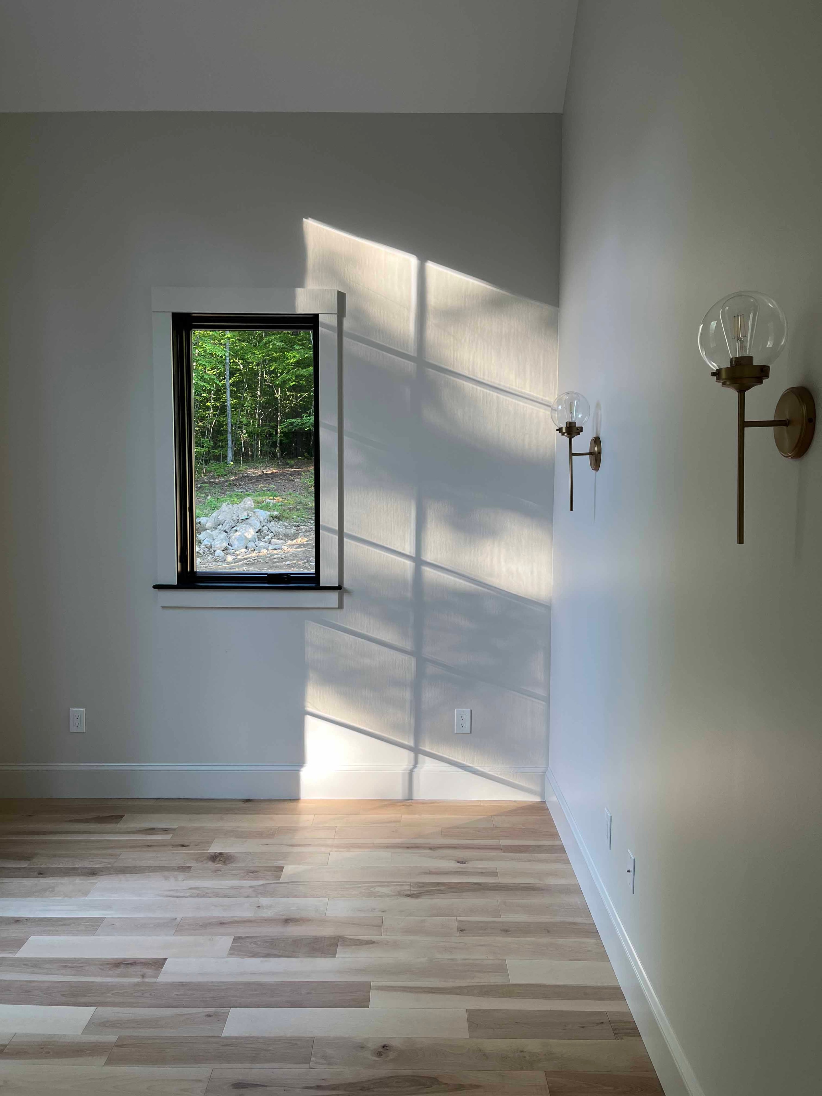 Holderness Home bedroom with black-framed window, brass globe sconces, and oak hardwood floors
