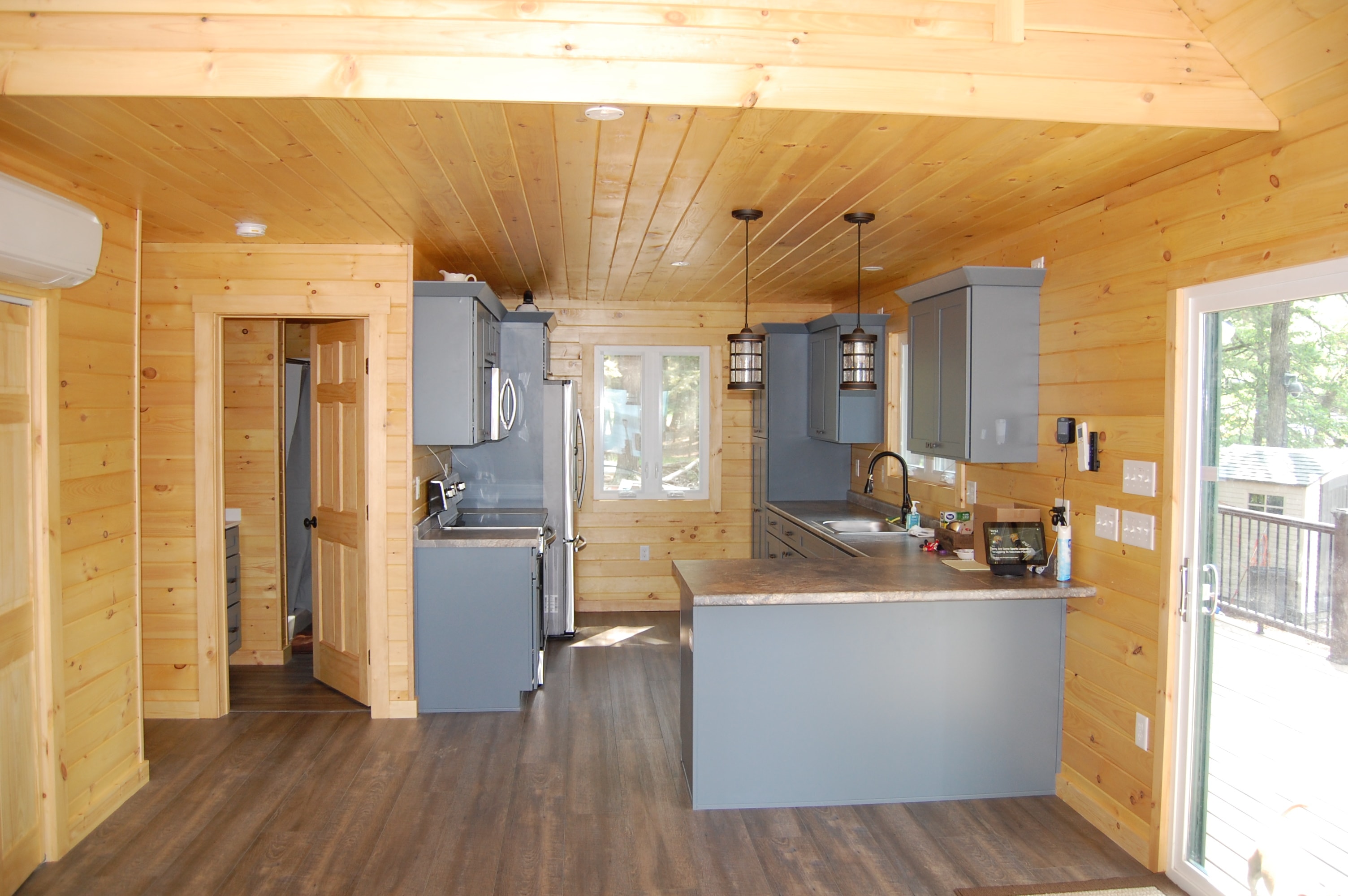 Island Retreat knotty pine kitchen with gray-blue shaker cabinets, granite countertops, stainless appliances, pendant lights, and dark LVP flooring — Welch Island, Laconia, NH