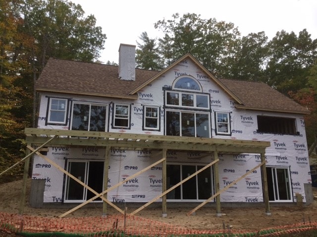 Lake Kanasatka Home exterior framing with Tyvek wrap, round attic window, deck framing, and autumn foliage — Moultonborough, NH