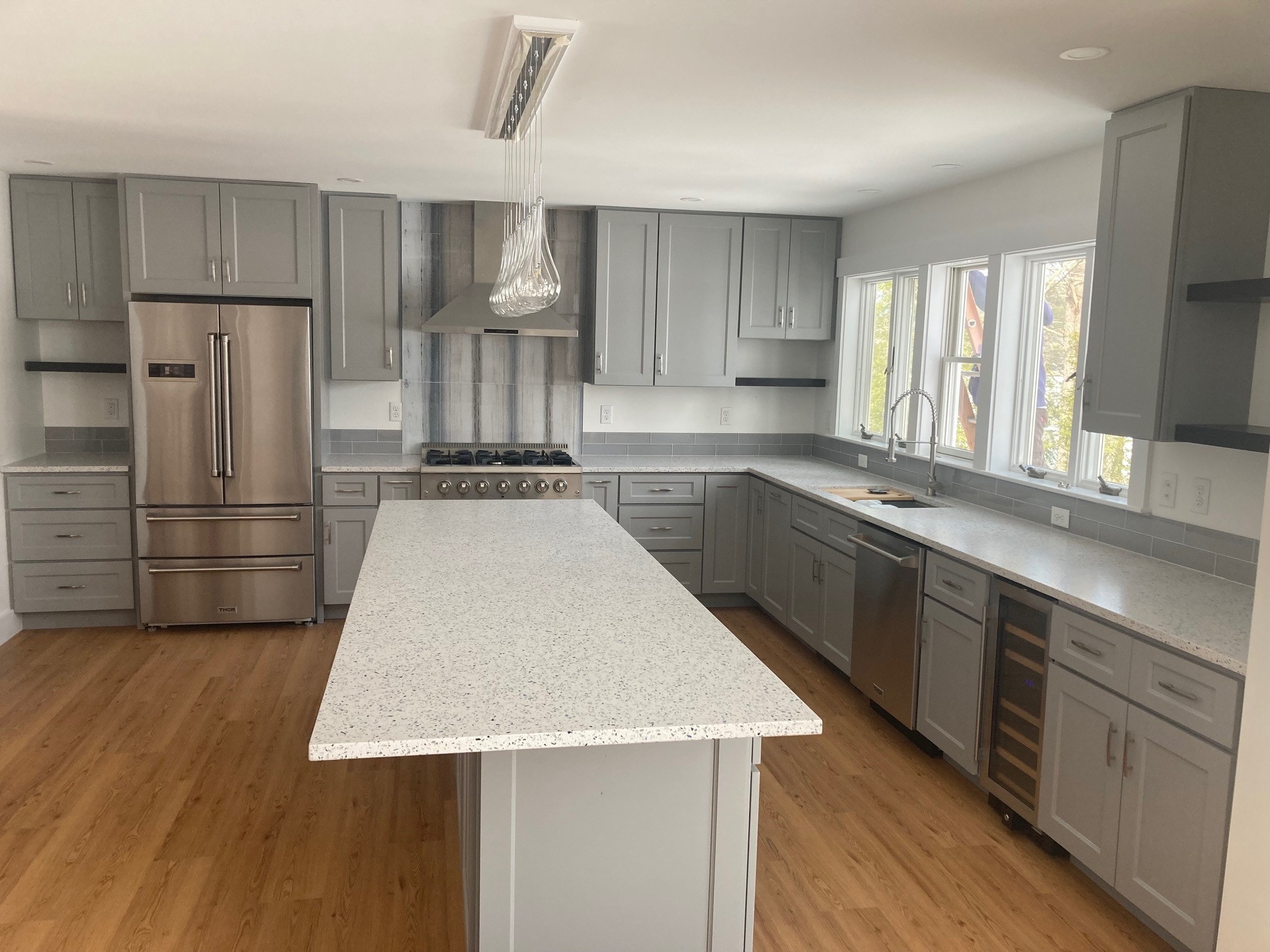 Lake Kanasatka Home kitchen with gray shaker cabinets, quartz island, Thor stainless appliances, and crystal pendant light — Moultonborough, NH