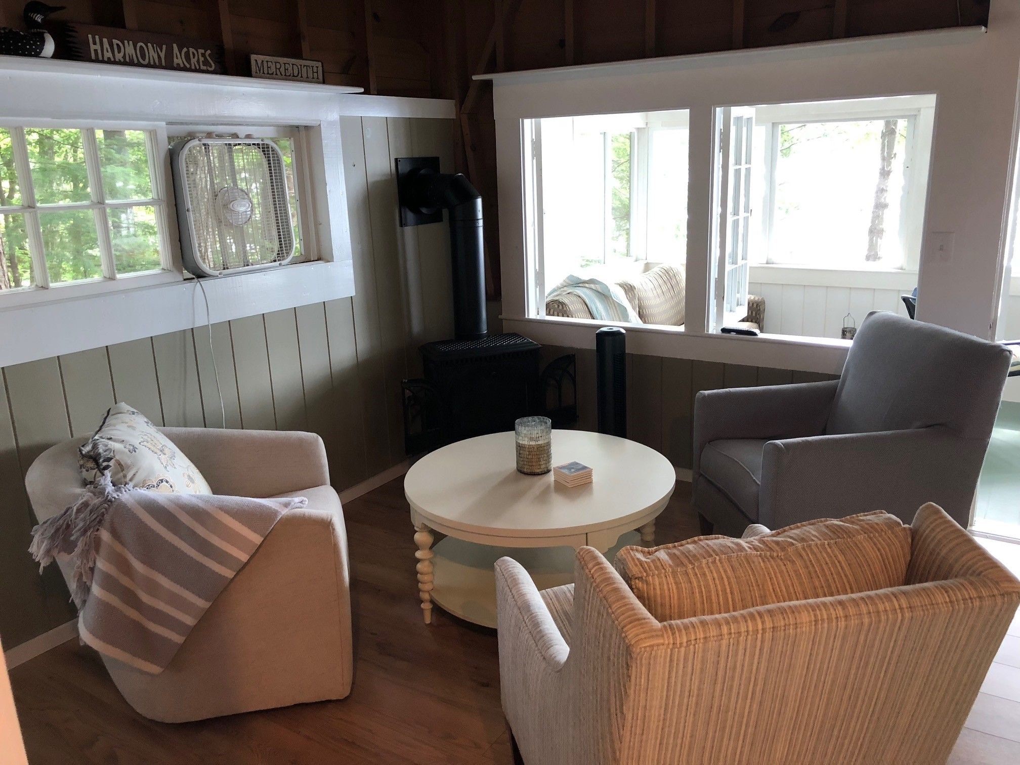 Loon Song Cottage living room with sage green shiplap walls, black wood stove, round white coffee table, and armchairs — Meredith, NH