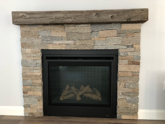 Mason New Build stacked stone fireplace with black frame insert, reclaimed wood beam mantel, and wide-plank floors — Governor's Crossing, NH