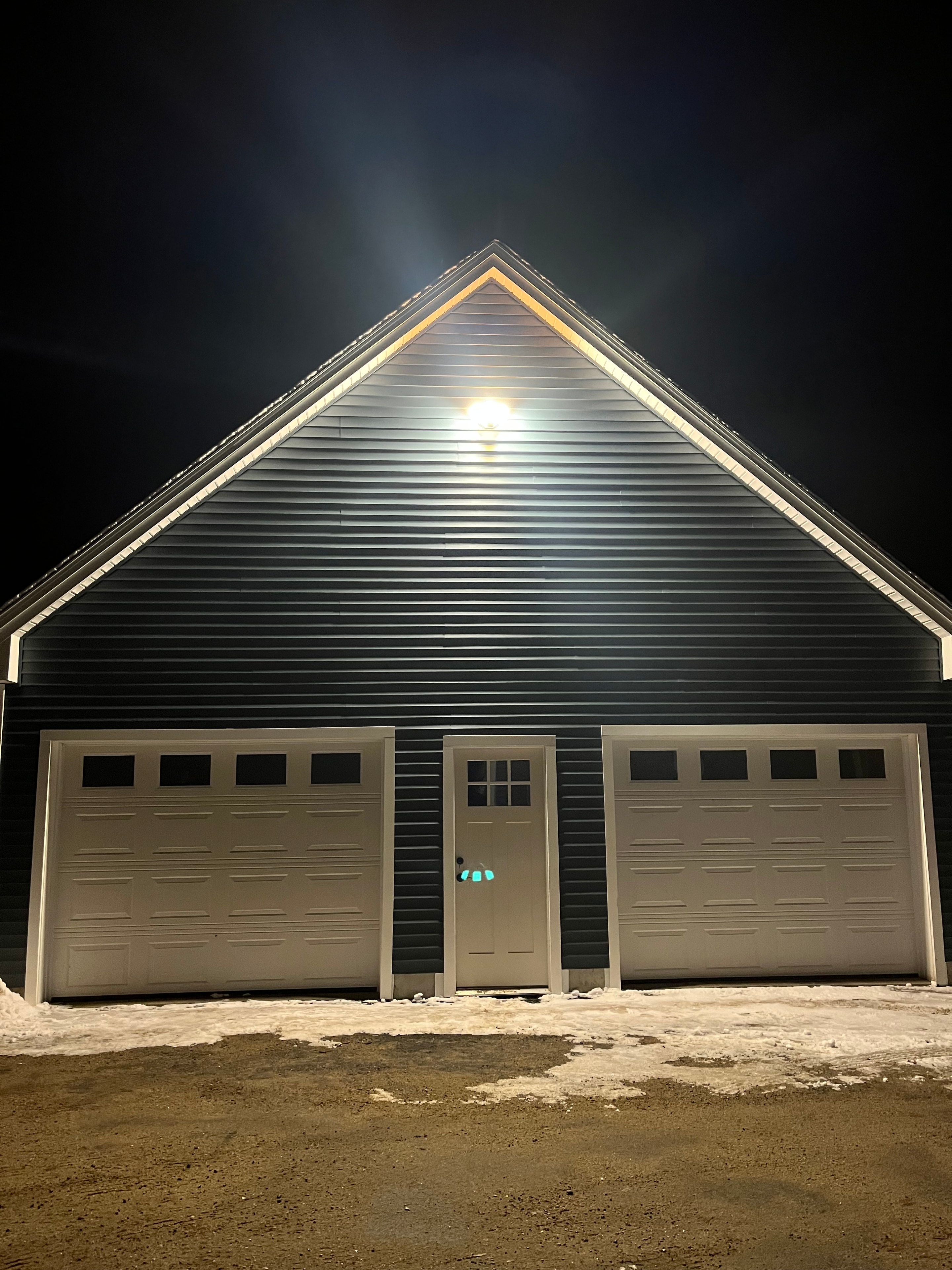 Mountain View Home dark corrugated metal exterior at night with illuminated double garage doors and entry door