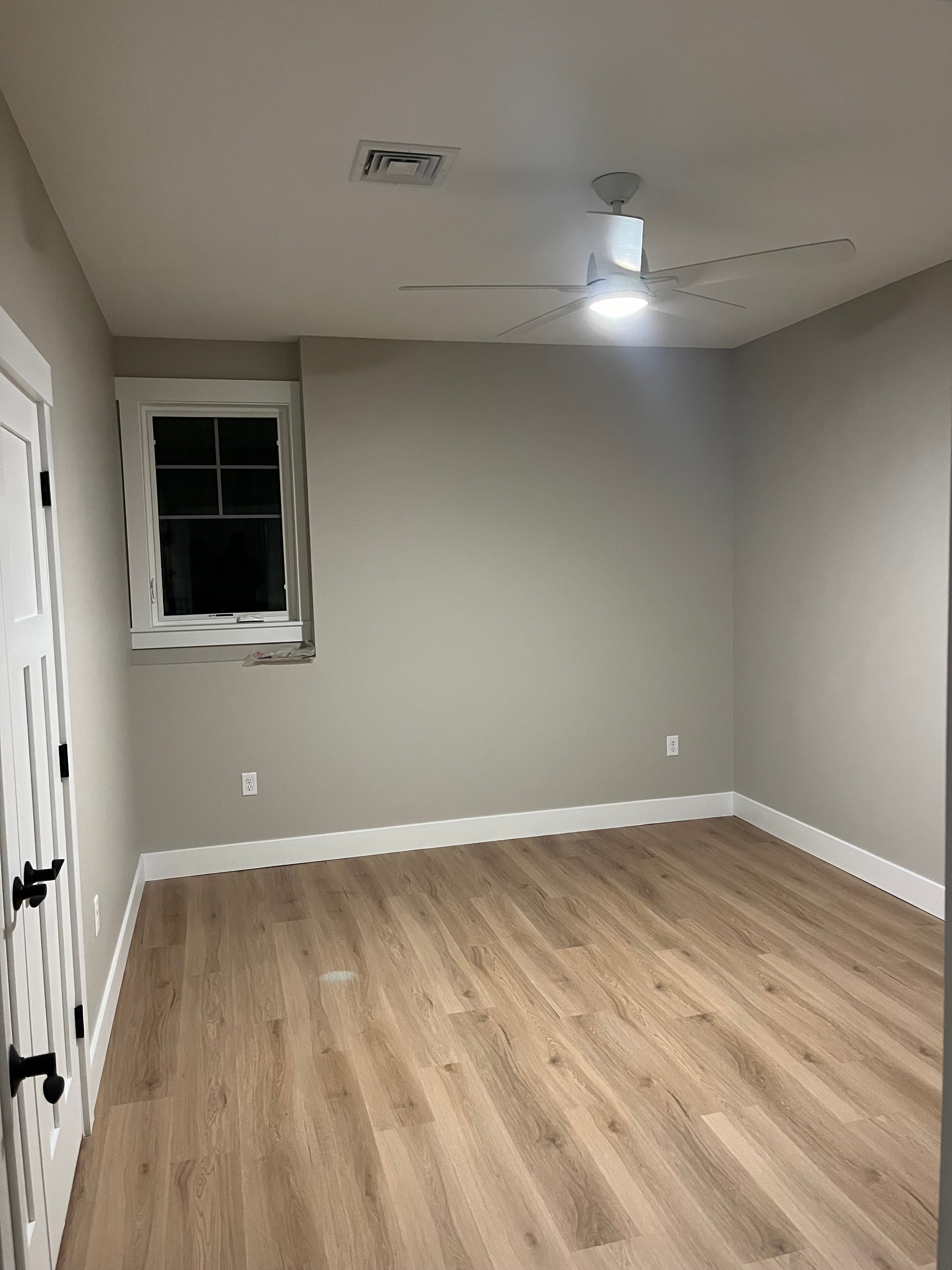 Mountain View Home bedroom with sage green walls, ceiling fan, single window, light oak LVP flooring, and black bath fixtures
