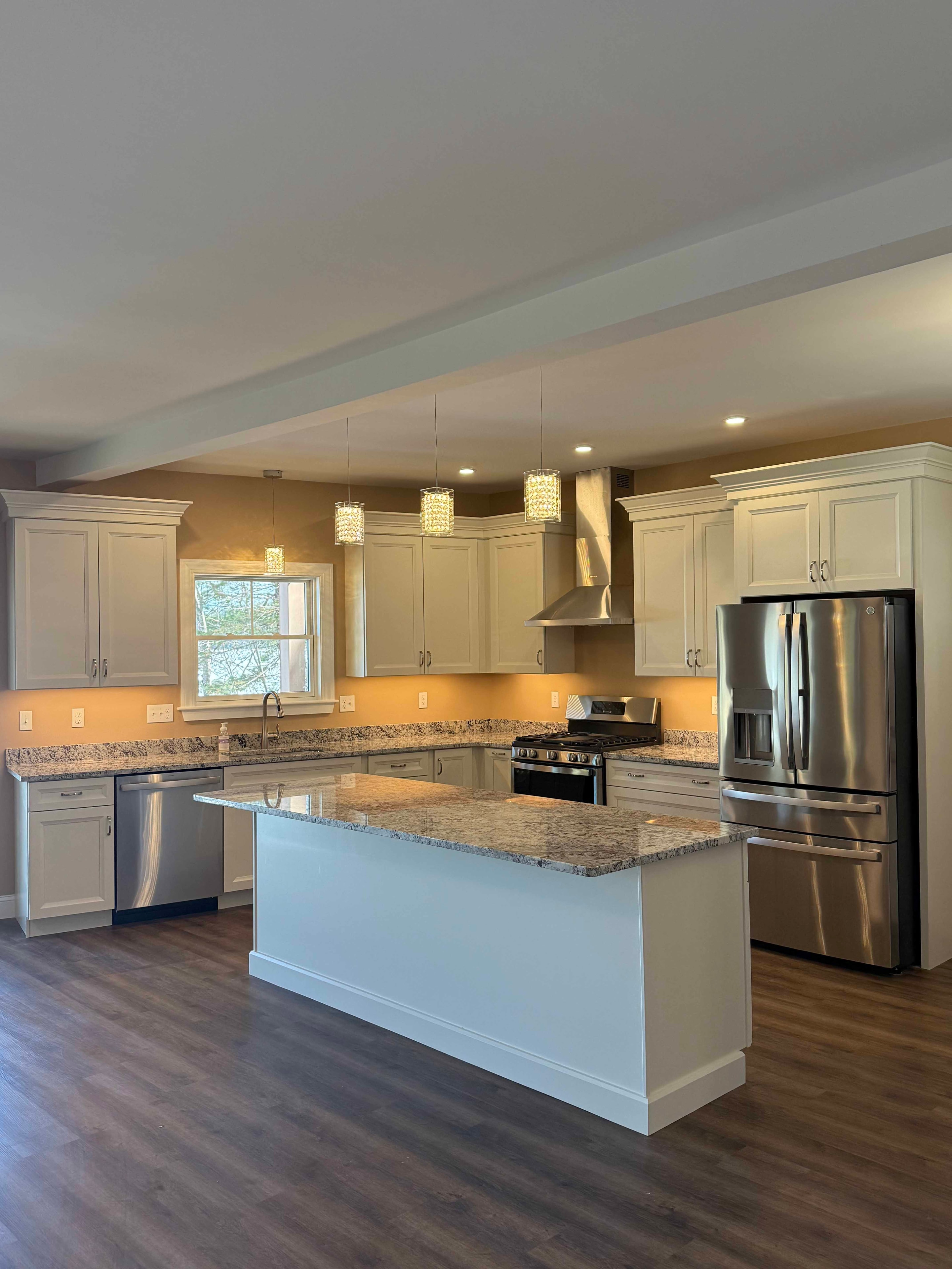 Squam Lake Home kitchen with white cabinets, granite island, stainless appliances, and pendant lights