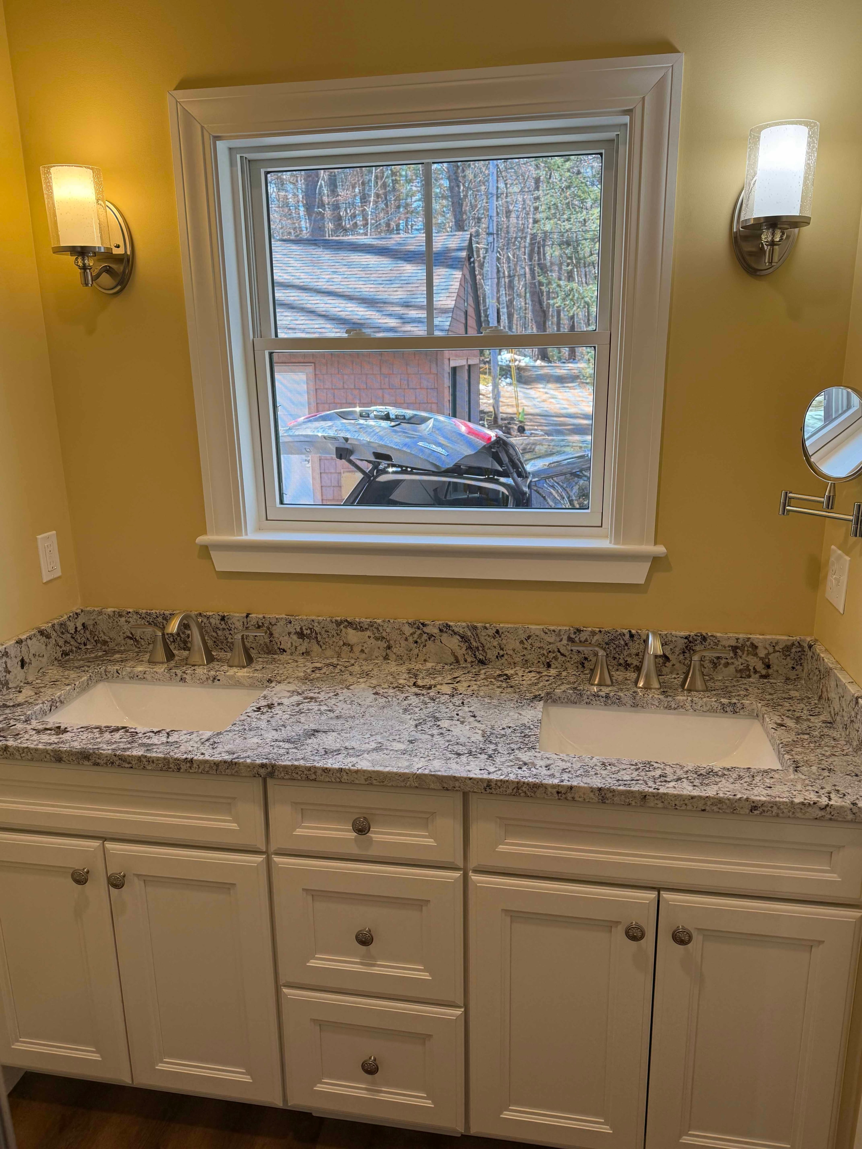 Squam Lake Home master bath double vanity with white cabinets, granite countertop, and window between sconces