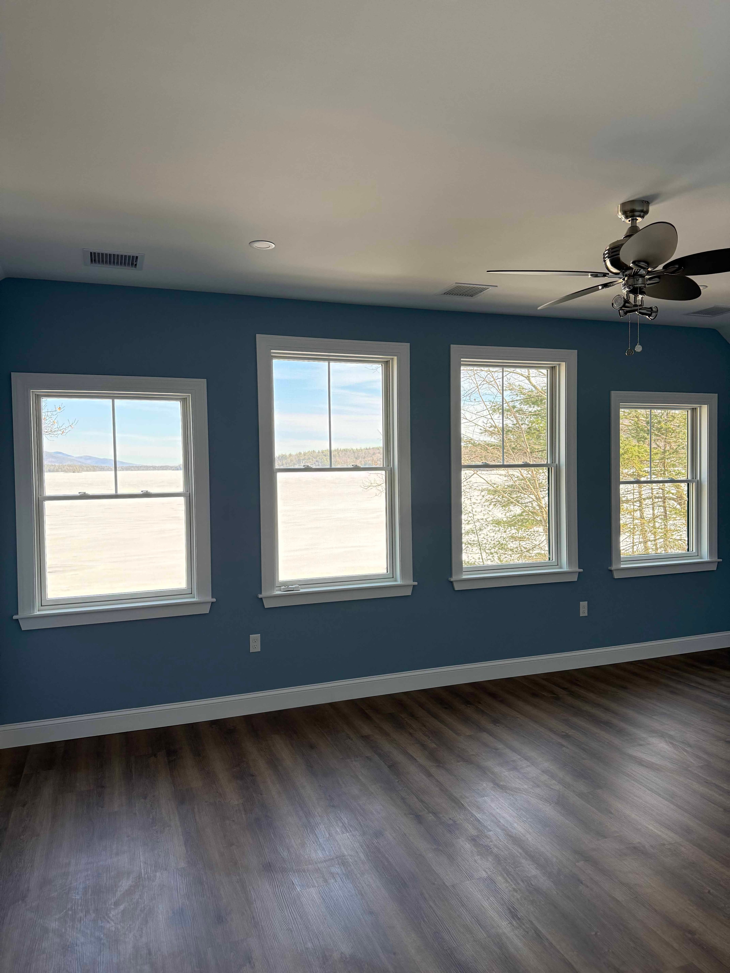 Squam Lake Home master bedroom with blue walls, ceiling fan, and lake-view windows