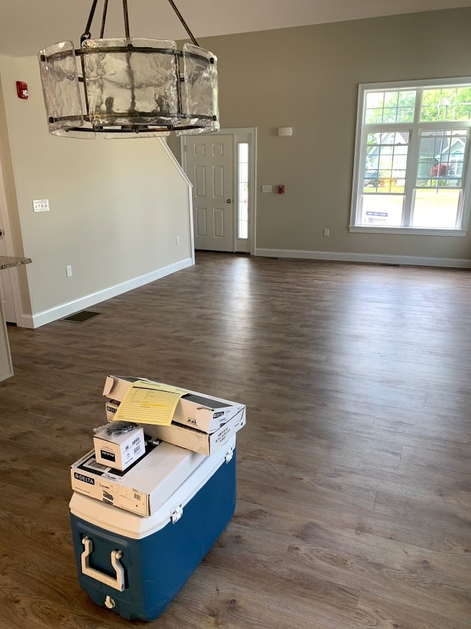Webster New Build open living and dining area with drum chandelier, wide-plank floors, and front door view — Governor's Crossing, NH