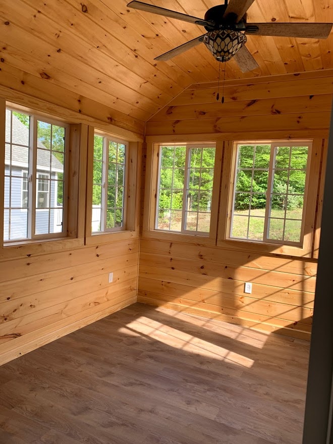 Webster New Build knotty pine sunroom with vaulted ceiling, ceiling fan, three windows overlooking wooded yard, and wide-plank floors — Governor's Crossing, NH