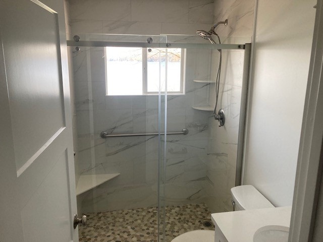 Lake Winnisquam Cottage Remodel bathroom with marble tile walk-in shower, sliding glass door, pebble floor, and chrome fixtures — Winnisquam, NH