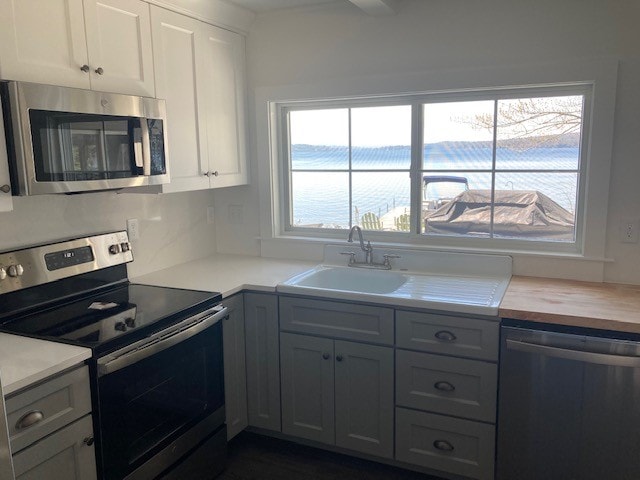 Lake Winnisquam Cottage Remodel kitchen with lake view window, farmhouse sink, stainless appliances, and quartz countertops — Winnisquam, NH